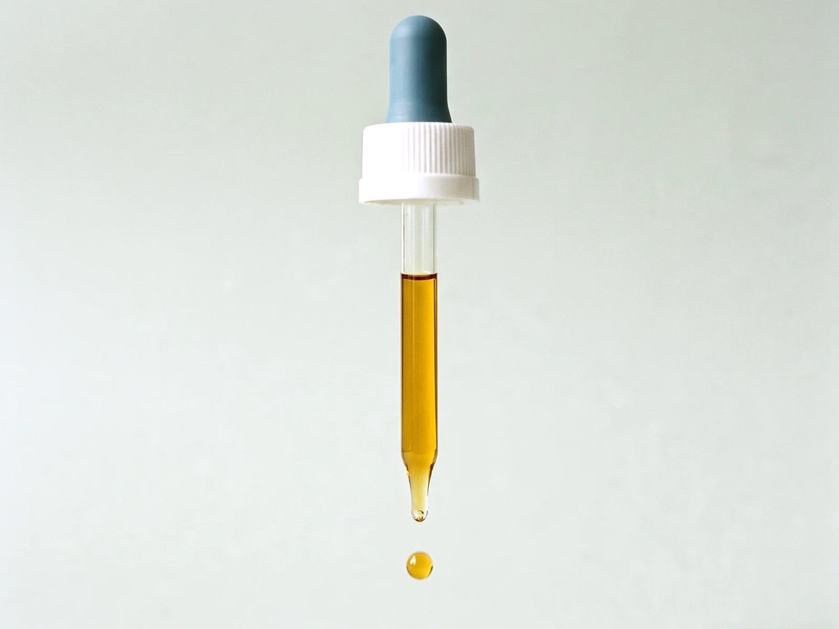 Conta-gotas com óleo âmbar soltando uma gota